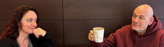 Deux comédiens sont assis à une table et se regardent